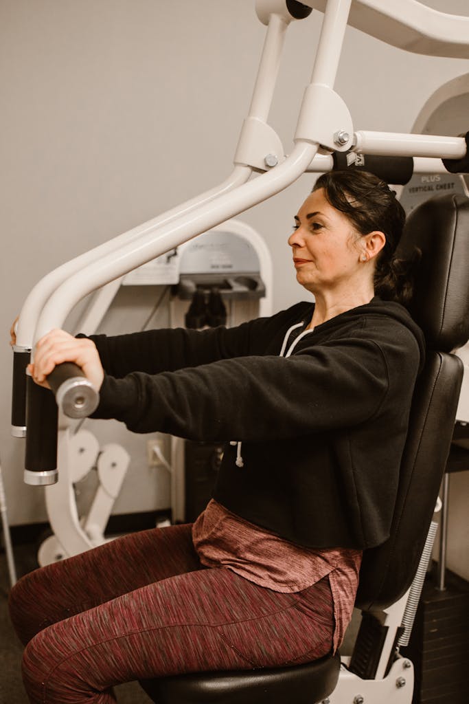 Middle-aged woman using a chest press machine in a gym for fitness.